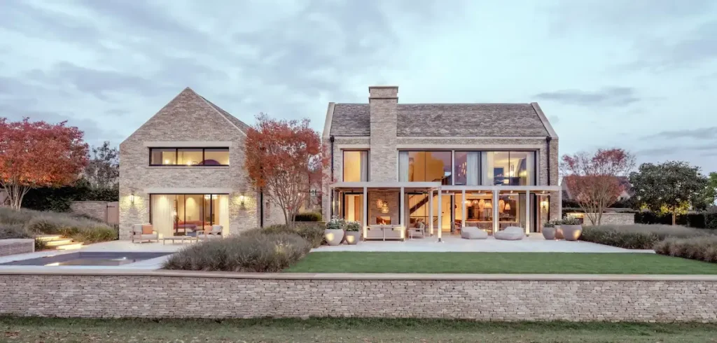 Luxury contemporary Cotswold stone home with large windows, terrace seating, and landscaped garden.