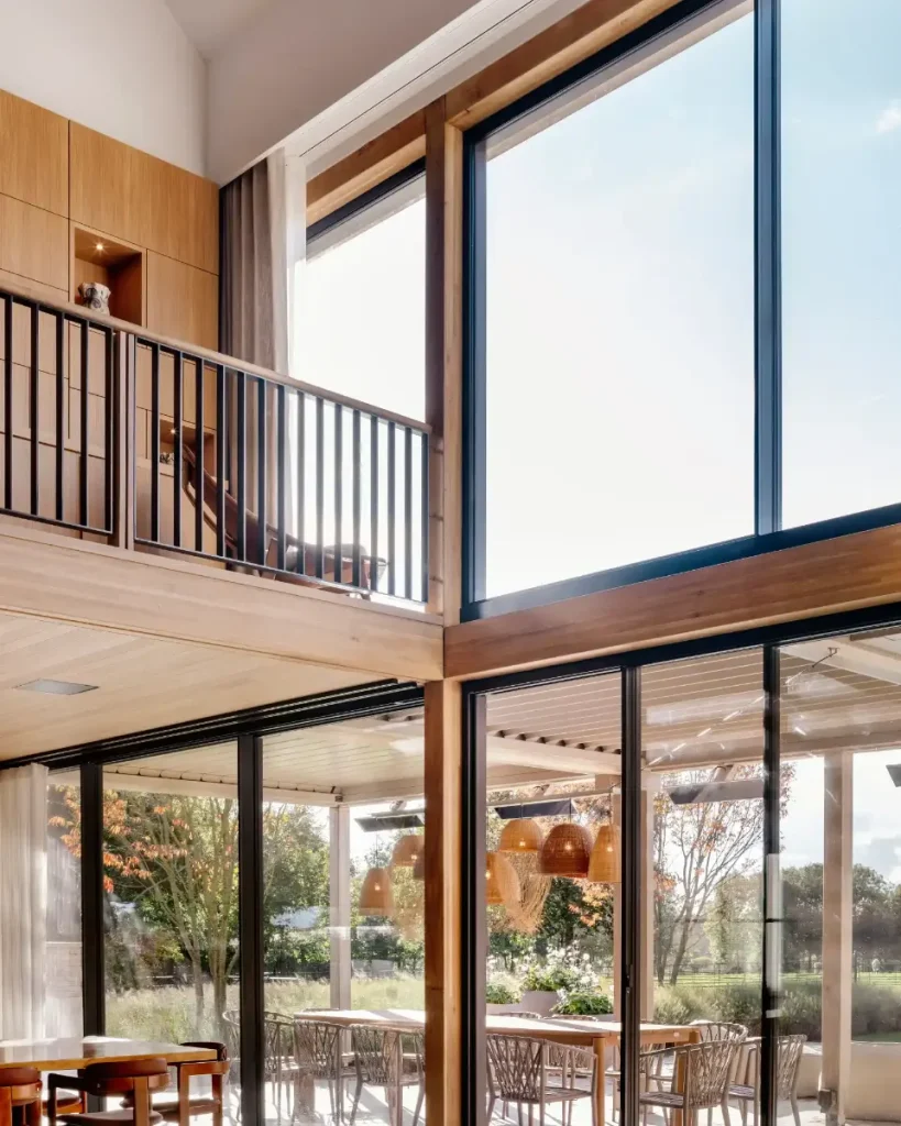 Double-height glazed corner with timber framing, mezzanine landing, and covered outdoor dining terrace.