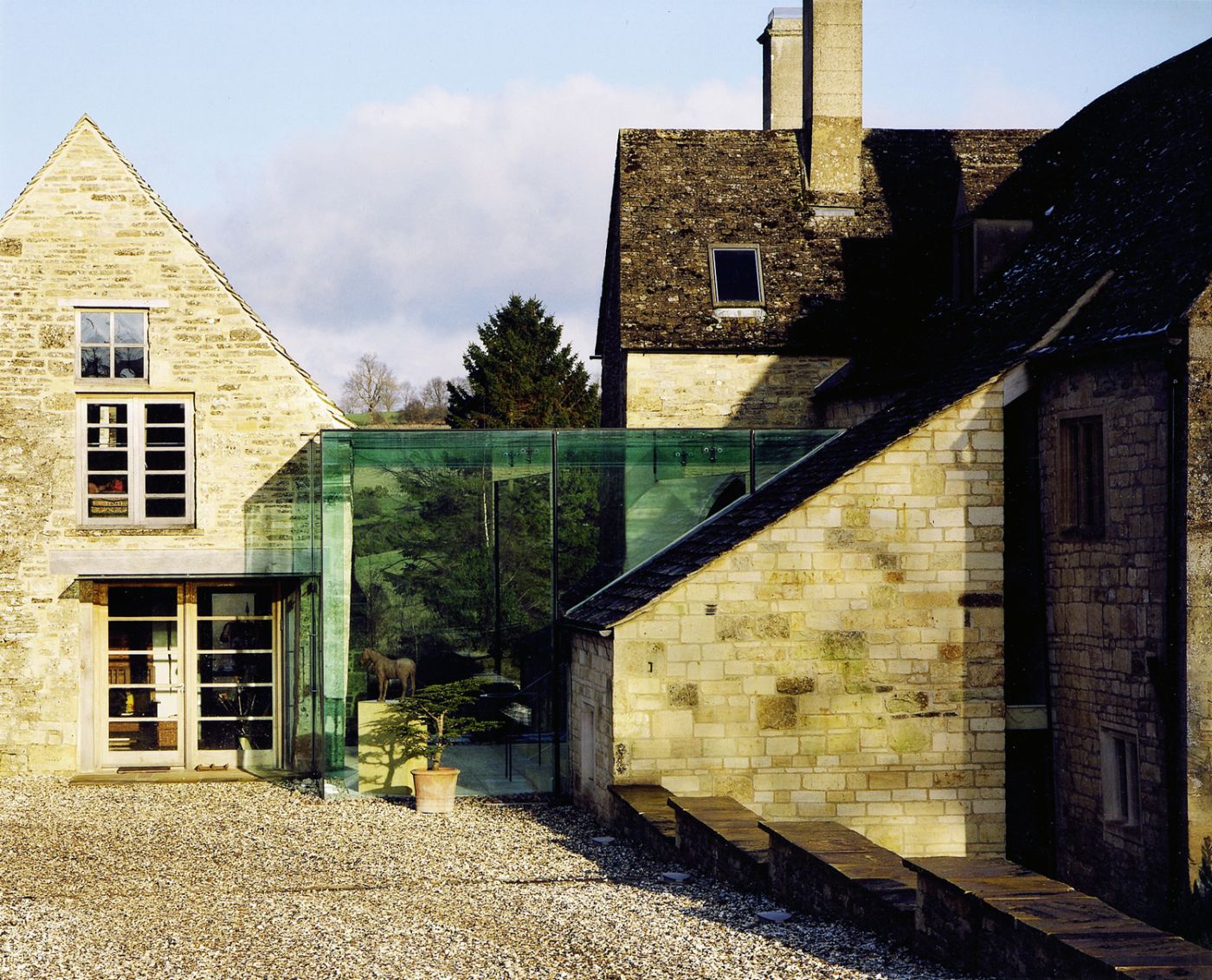 A new build Cotswold stone house that has a green glass featured in the image.
